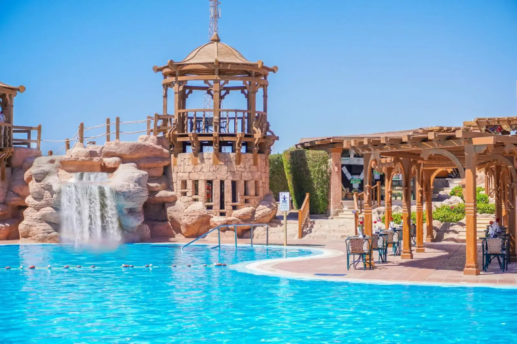 Charmillion Sea Life Resort: A bright outdoor pool with a rock waterfall and shaded seating beneath a timber pergola.