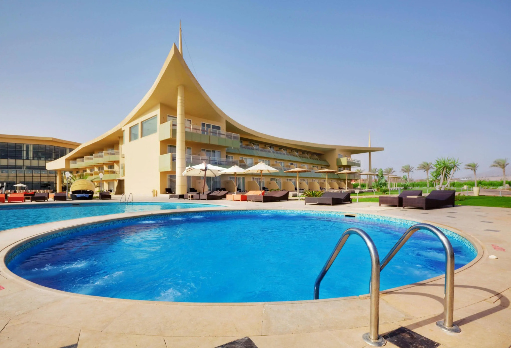 Barceló Tiran Sharm: A curved outdoor swimming pool sits beside a spacious sun deck with loungers and umbrellas.