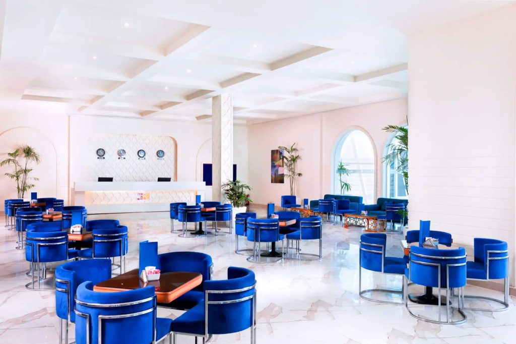 Pickalbatros Palace Sharm & Aqua Park: A bright indoor lounge with blue upholstered seating, tables, and a long counter.