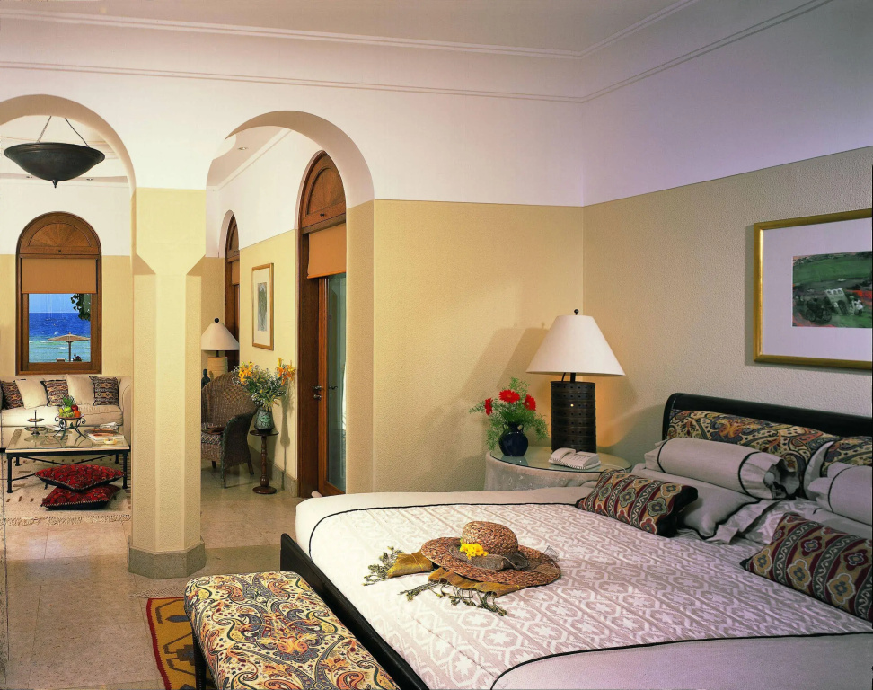 صورة: The Oberoi Beach Resort, Sahl Hasheesh: An elegant bedroom with a patterned bed, decorative pillows, and a separate sitting area framed by arched windows.