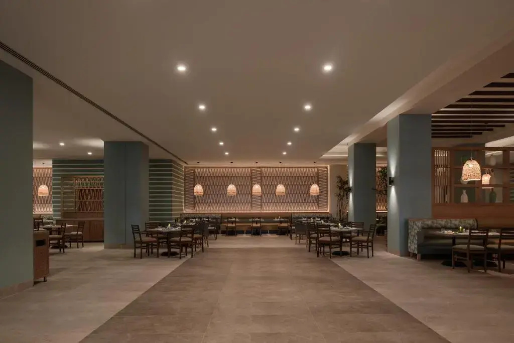 JAZ Elite Asteria Hotel: A spacious dining room with neatly arranged tables, booth seating, and warm pendant lighting.