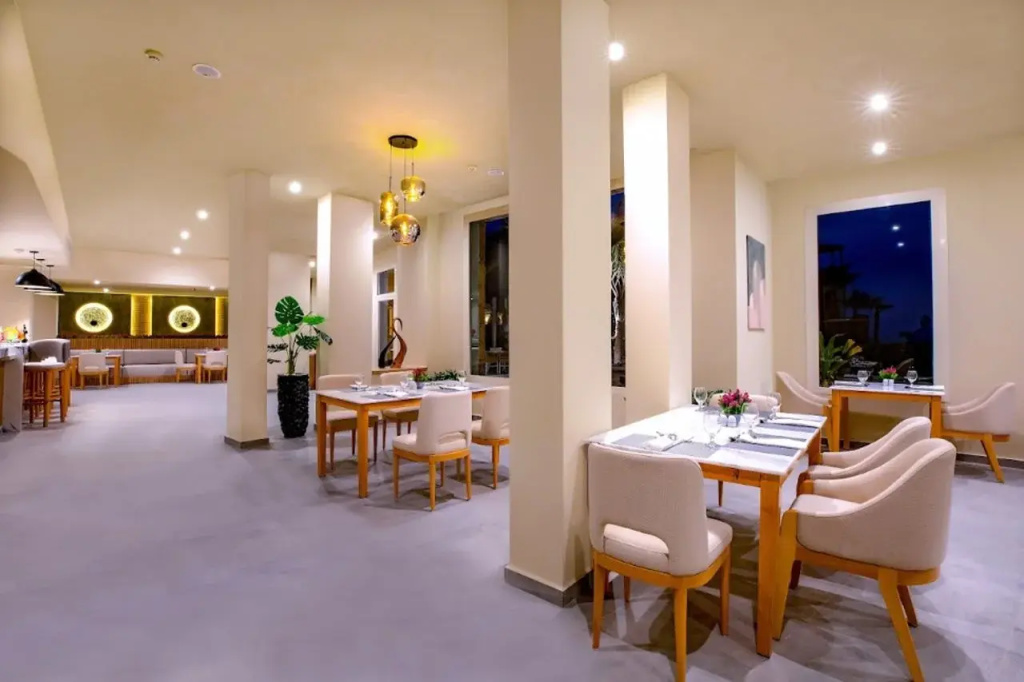 AJIRA Resort Sahl Hasheesh: A spacious dining area with neatly arranged tables, upholstered chairs, and a bar counter.