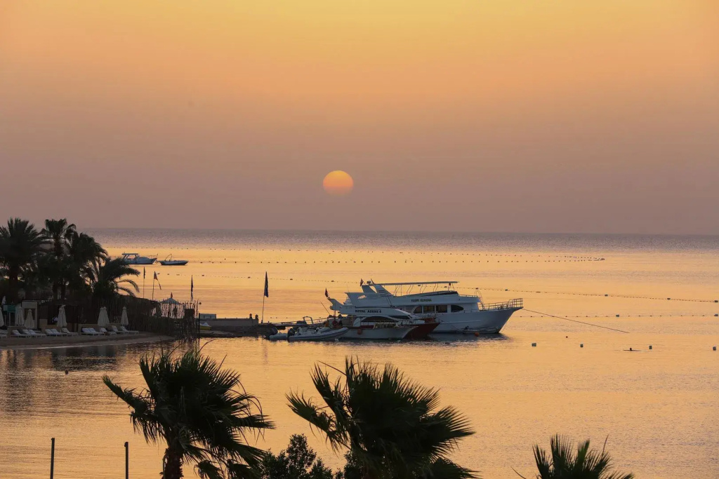 Xanadu Makadi Bay - High Class All Inclusive: Sunset over the sea, with boats offshore and palm trees silhouetted in the foreground.