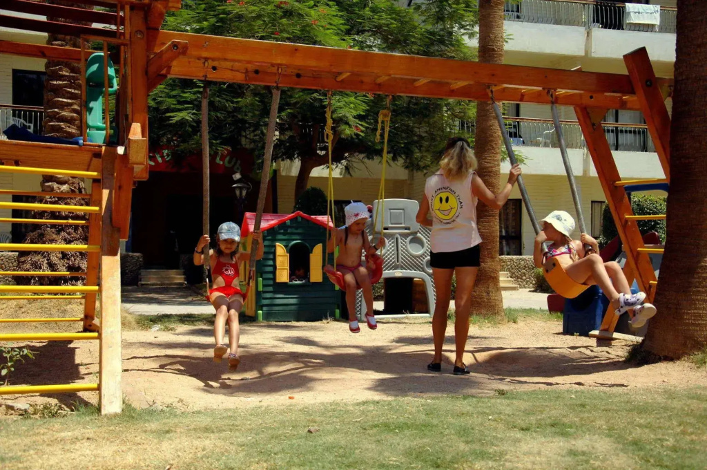 Regina Resort and Aqua Park Hurghada: Children enjoy swings beneath a wooden playground structure in a sunny outdoor play area.