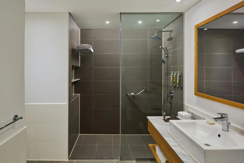 Renaissance Sharm El Sheikh Golden View Beach Resort: A modern bathroom with a dark-tiled walk-in shower, handheld showerhead, and vanity basin.