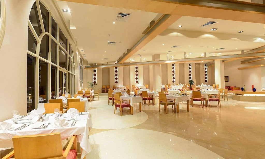 Prima Life Makadi Hotel - All inclusive: Spacious restaurant dining room with neatly set tables, upholstered chairs, and tall windows.