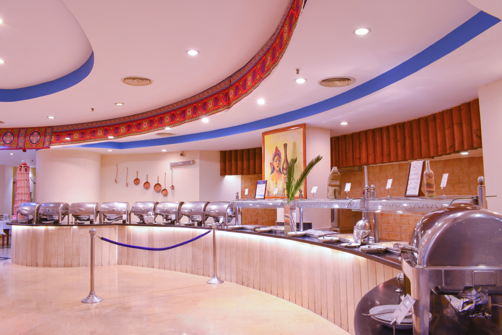 Parrotel Beach Resort: A spacious buffet area features a curved serving counter with stainless-steel chafing dishes and warm decorative details.