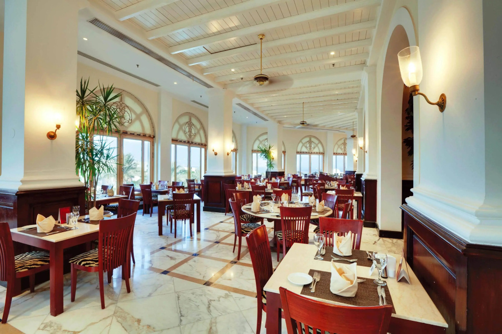 Savoy Sharm El Sheikh hotel: A bright, spacious restaurant dining room with set tables, wooden chairs, and tall arched windows.