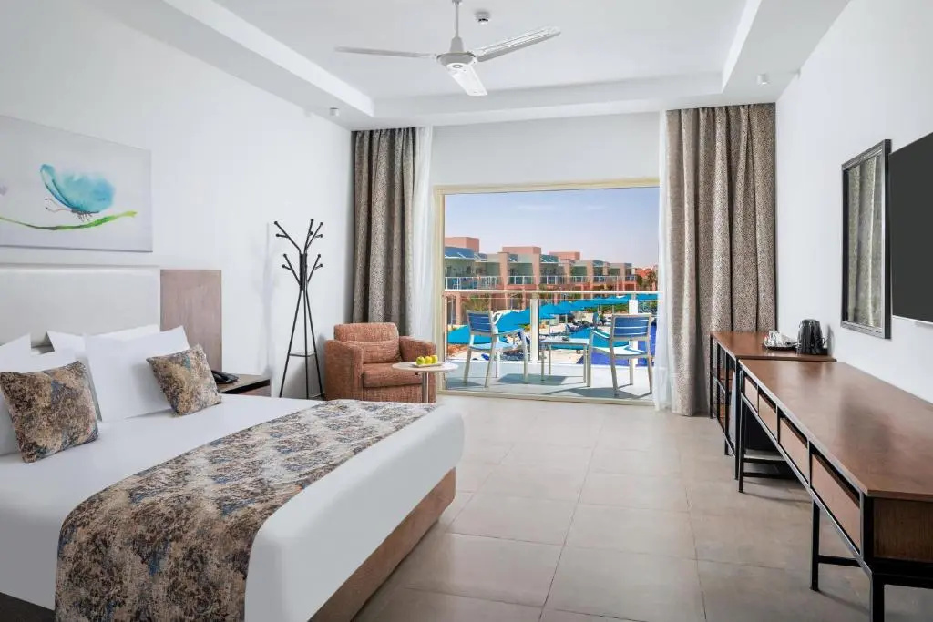 Albatros Makadi Resort: A bright guest room with a seating area and large glass doors overlooking the resort pool.