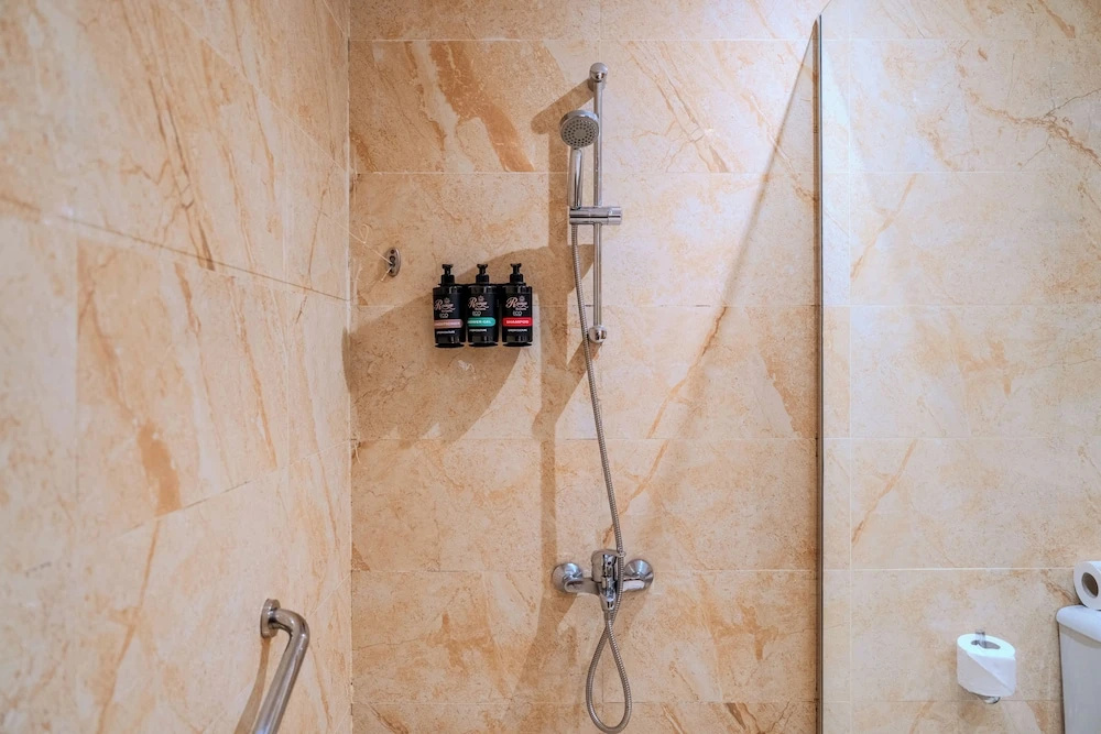 Rewaya Inn Resort: A bright tiled bathroom with a handheld shower, wall-mounted toiletries, and a grab bar.