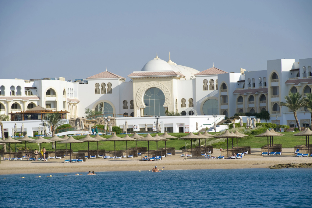 Old Palace Sahl Hasheseh: A beachfront hotel overlooks a sandy shore lined with sun loungers and parasols.