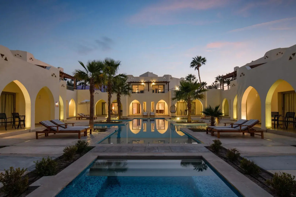Xanadu Makadi Bay - High Class All Inclusive: A palm-lined courtyard pool with sun loungers, framed by warmly lit hotel buildings.