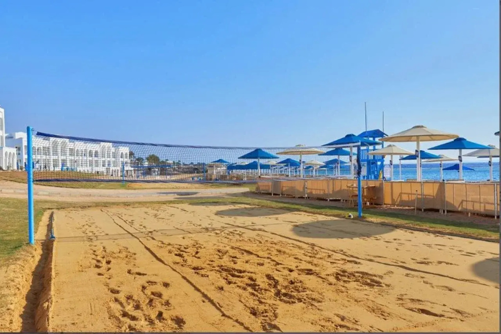 Pickalbatros Palace Resort - Sharm El Sheikh: A broad sandy area leads toward the resort’s white buildings and a deck lined with blue shade canopies.