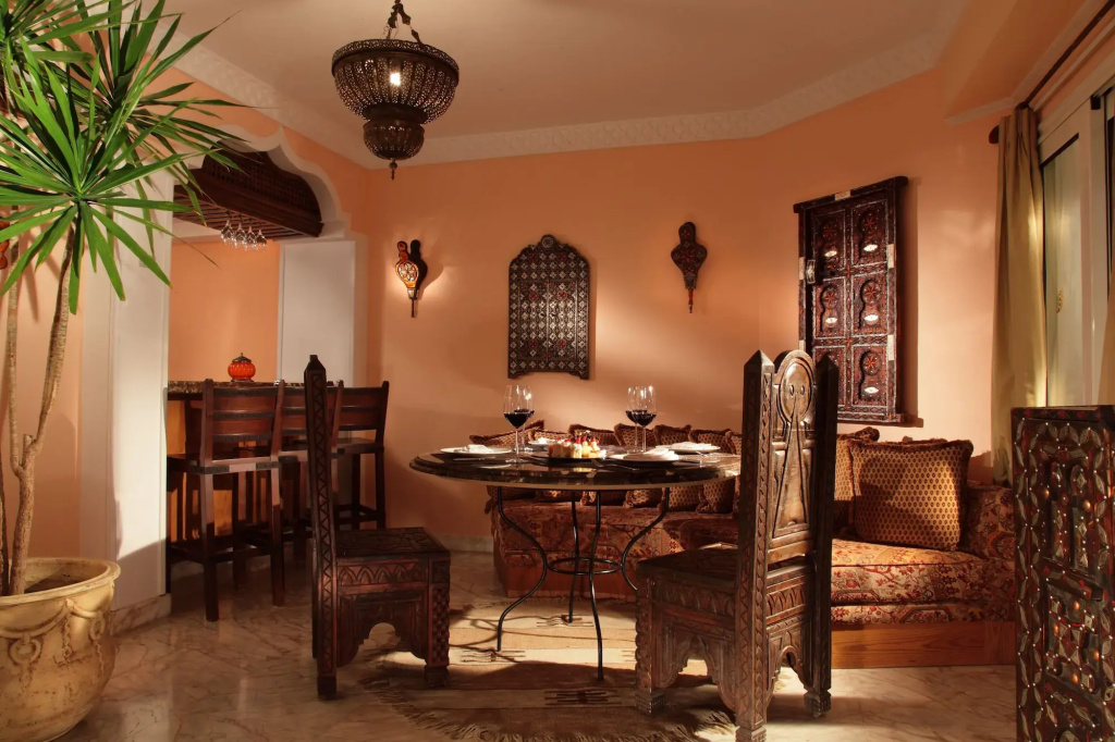 Royal Savoy Sharm El Sheikh: An ornate dining area with a set table, carved wooden chairs, and a cushioned bench.