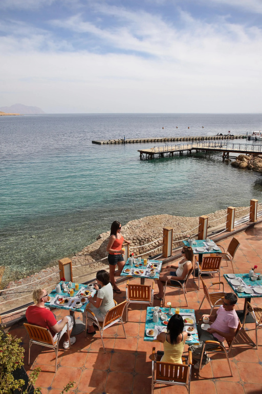 Lido Sharm Hotel Naama Bay: Dine outdoors on a waterfront terrace overlooking clear turquoise water and a pier.