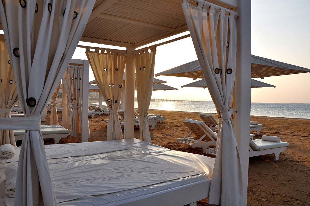 KaiSol Romance Resort Sahl Hasheesh (Adults Only): A shaded beach cabana with a cushioned daybed sits beside sun loungers overlooking the sea.