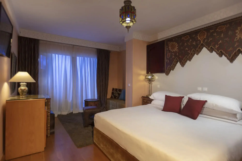 Royal Savoy Sharm El Sheikh: A warmly lit bedroom with a large bed, a cozy seating area, and ornate decorative details.