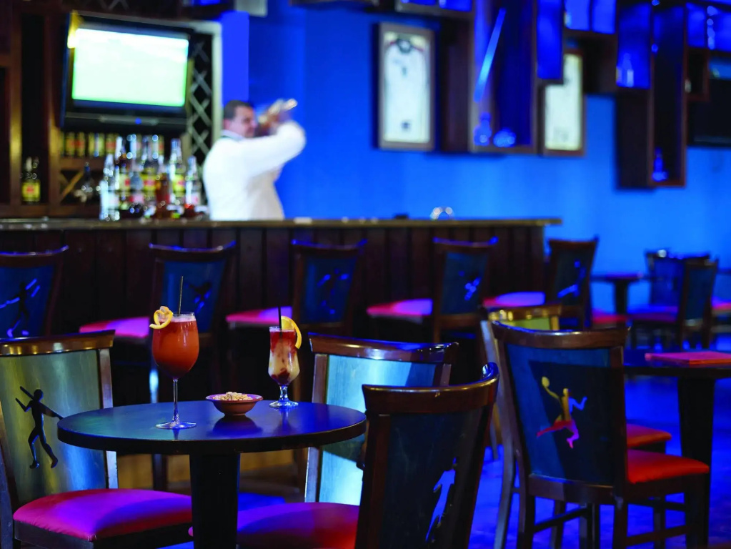 صورة: Coral sea Holiday Resort & Aqua park: A dimly lit bar lounge with colorful accent lighting, cocktail tables, and drinks served at the bar.
