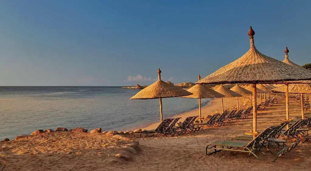 Park Regency Sharm El Sheikh Resort: Relax on the sandy beachfront beneath thatched parasols, with rows of loungers beside the calm sea.