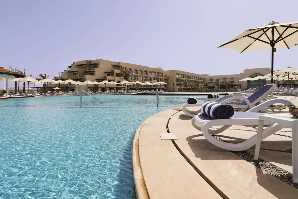 Mövenpick Waterpark Resort & Spa Soma Bay: An outdoor resort pool is lined with sun loungers and shaded by large parasols.