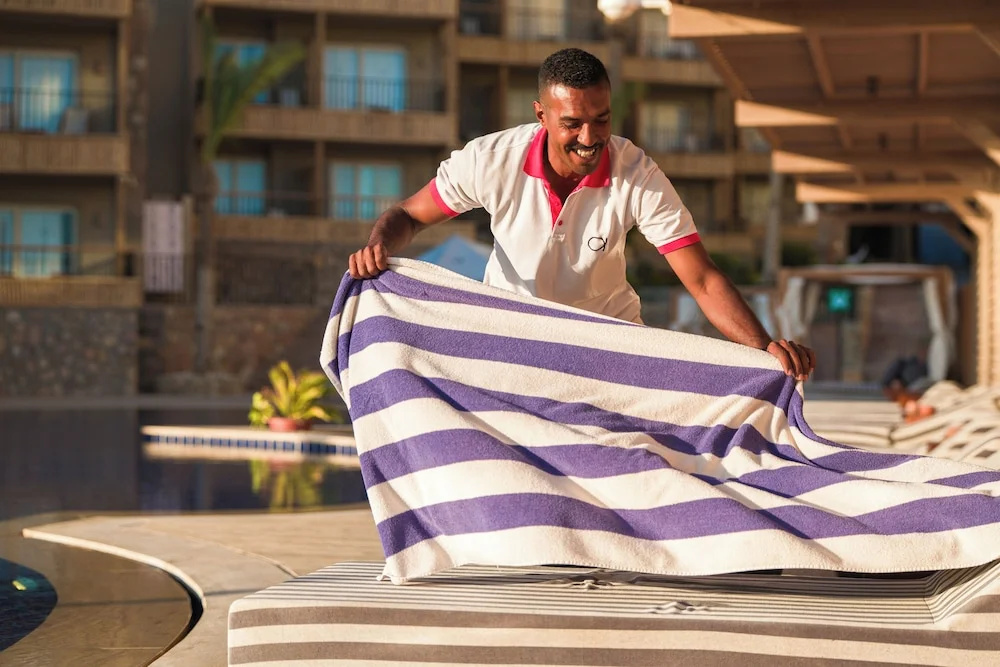 ananea Hurghada – Adults Only: A staff member displays a striped towel beside the hotel pool.