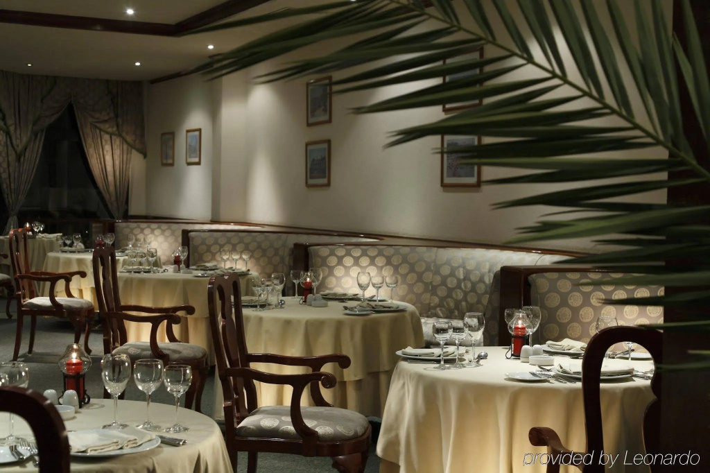 Pharaoh Azur Resort: An elegant indoor dining room with linen-covered tables, set with glassware and surrounded by upholstered banquettes and dark wood chairs.