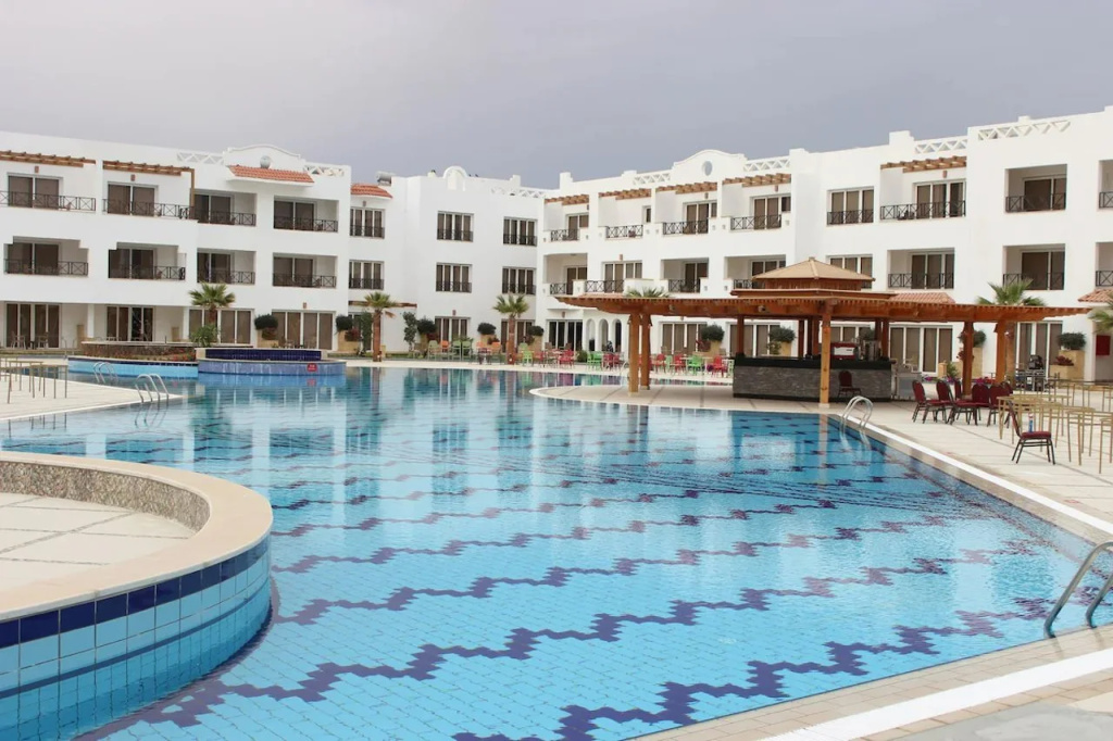 Old Vic Sharm Resort: A large outdoor pool sits beside the resort buildings, with poolside seating and a covered bar area.