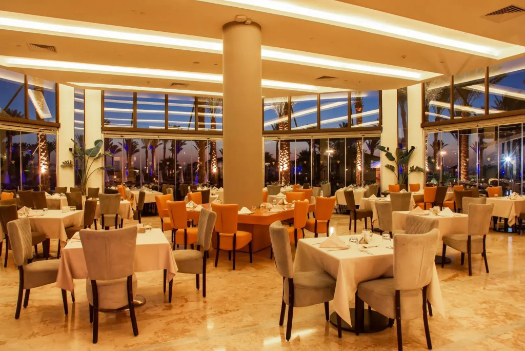 Rixos Sharm El Sheikh Ultra All Inclusive - Adults Friendly: A spacious restaurant dining room with neatly set tables, upholstered chairs, and floor-to-ceiling windows.