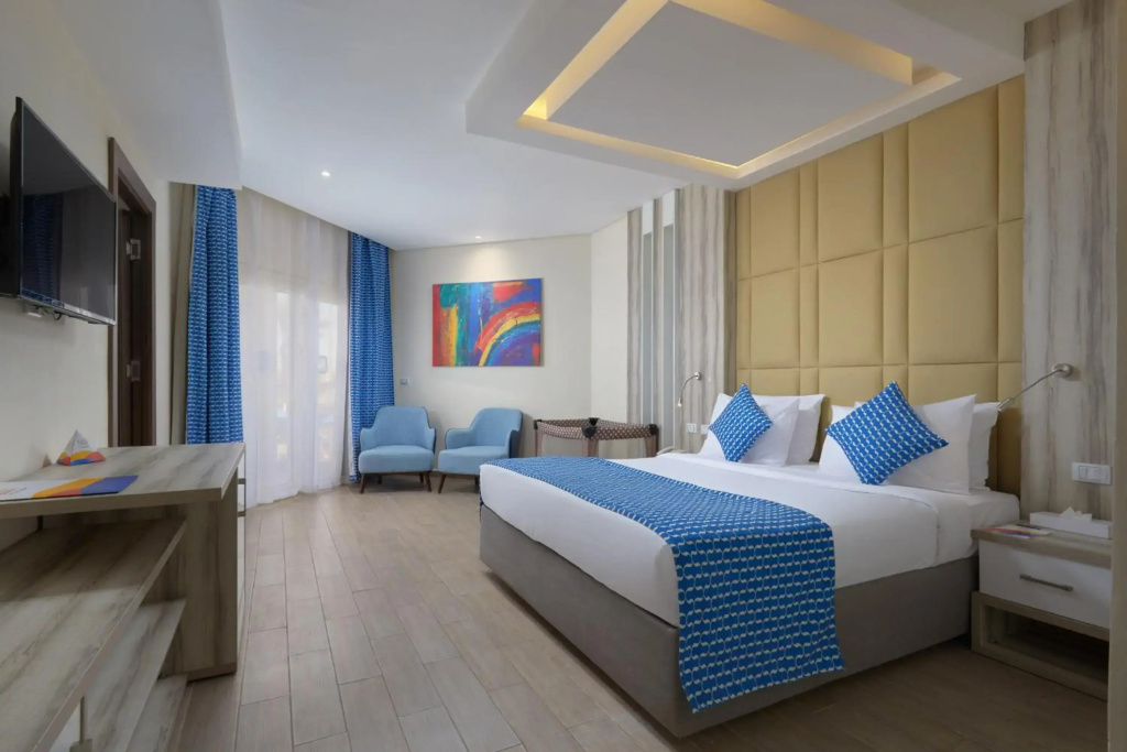 Bellagio Beach Resort & Spa: A bright guest room with a king-size bed, a wall-mounted TV, and a pair of lounge chairs.