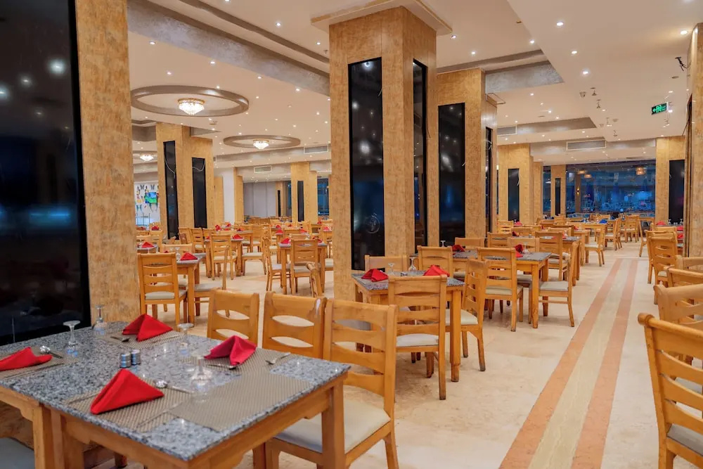 Rewaya Inn Resort: Spacious dining room with rows of wooden chairs and tables set with red napkins.