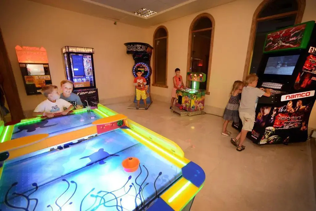 Charmillion Club Aqua Park: An indoor arcade features an air hockey table and a row of colorful video game cabinets.