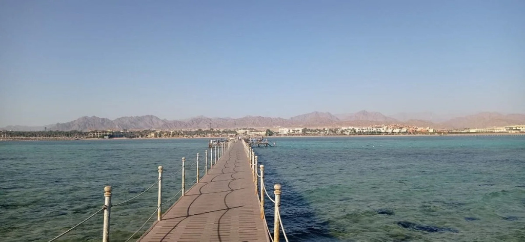 Romance Regency Club Adult Only (+16) - Ultra All Inclusive: A long pier stretches over calm blue water toward the distant shoreline.