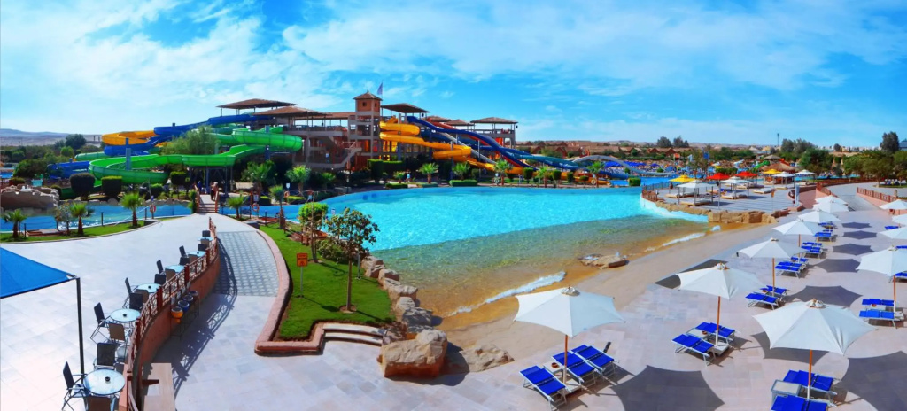 Pickalbatros Jungle Aqua Park - Neverland Hurghada: A large lagoon-style pool sits beside a sandy beach area, with colorful water slides and shaded sun loungers.