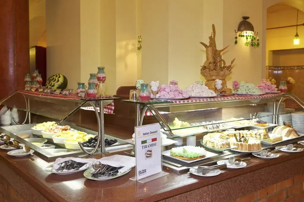Three Corners Rihana Resort: A dessert buffet features cakes, pastries, and plated sweets under warm indoor lighting.