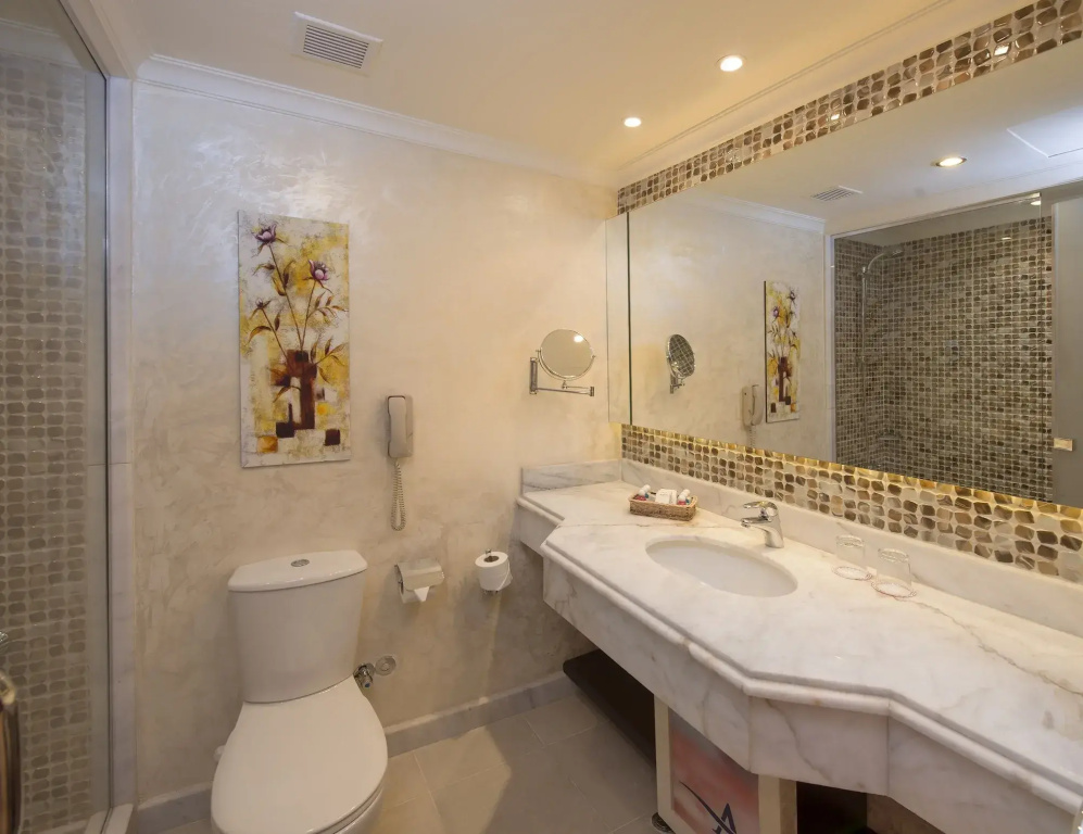 صورة: Amwaj Oyoun Resort & Casino Resort: A spacious bathroom with a long vanity, large mirror, toilet, and tiled shower area.