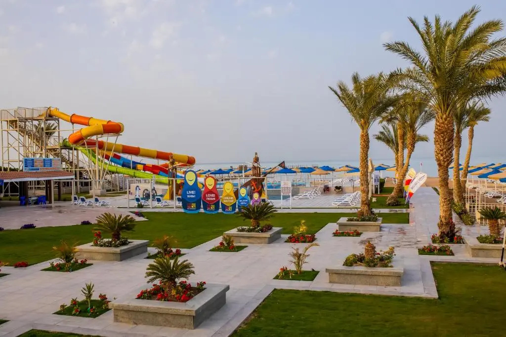 Bellagio Beach Resort & Spa: Palm-lined resort grounds lead to a beach area with loungers, umbrellas, and colorful waterslides.