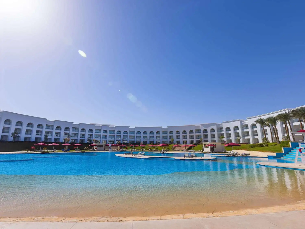Club Prive By Rixos Sharm El Sheikh: A large outdoor pool with sun loungers and red umbrellas sits in front of the hotel.