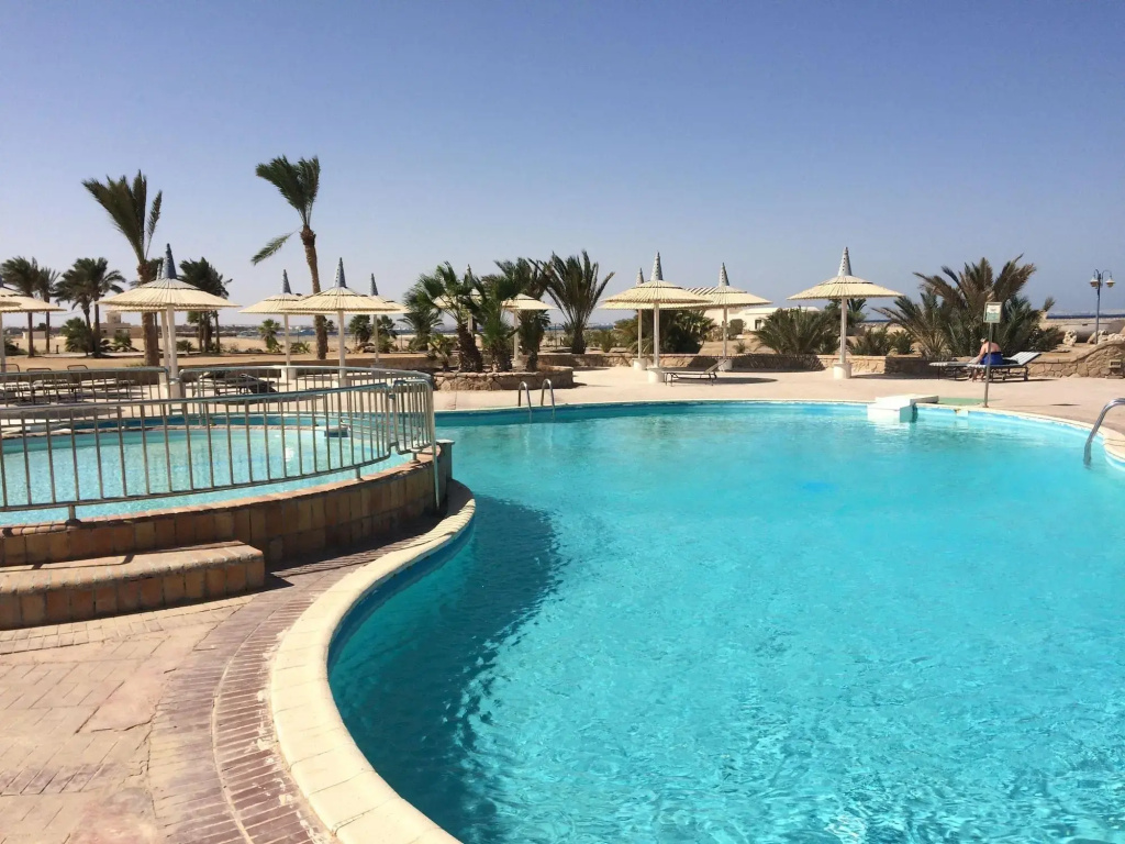 Coral Beach Resort: A spacious outdoor pool is bordered by a paved deck, sun loungers, and parasols, with palm trees beyond.