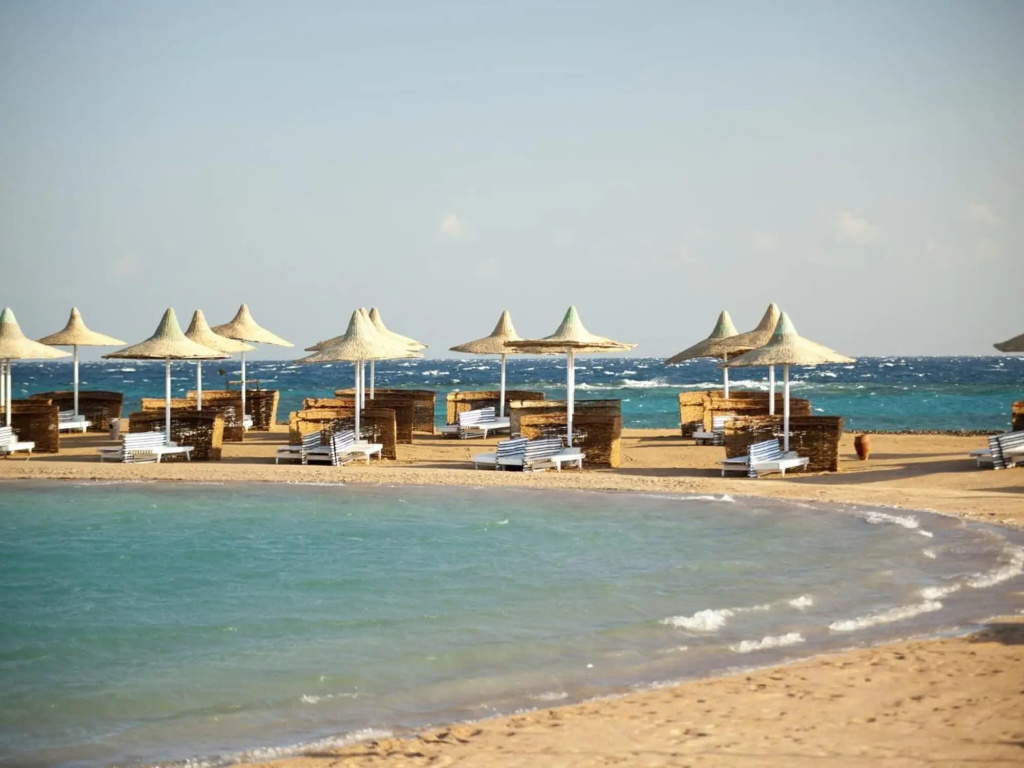 Coral Beach Resort: Relax on a sandy beachfront with sun loungers, shaded parasols, and cabana-style screens.