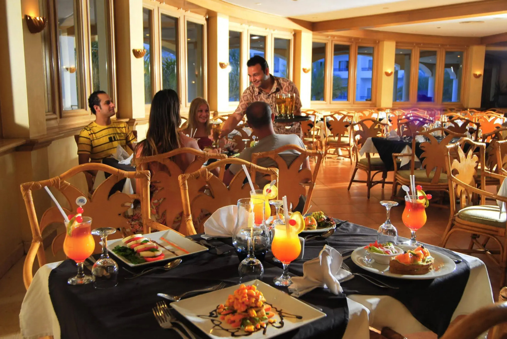 Naama Bay Hotel & Resort: A warmly lit dining room with table service, plated food, and colorful drinks.