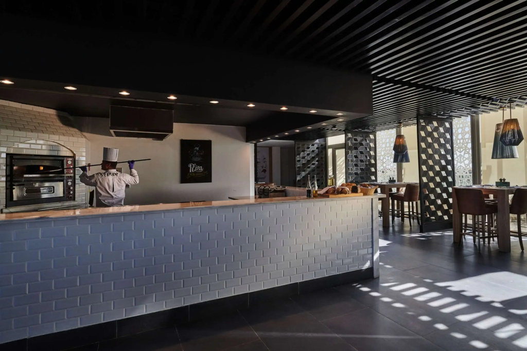 Steigenberger Pure Lifestyle (Adults Only): A modern restaurant features a long service counter, food displays, and bar-height seating.