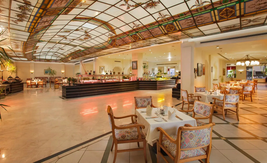 Pickalbatros Golf Beach Resort: A spacious restaurant with a long service counter, tiled floors, and comfortable dining tables beneath a decorative glass ceiling.