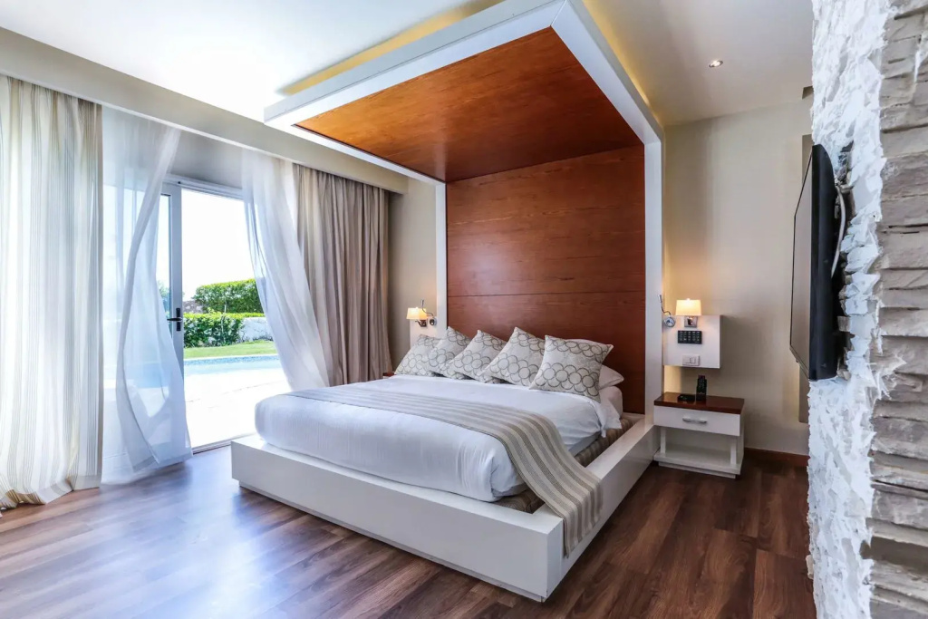 SUNRISE Montemare Resort - Grand Select: Bright bedroom with a king-size bed, wood accents, and sliding doors opening toward a pool and garden.