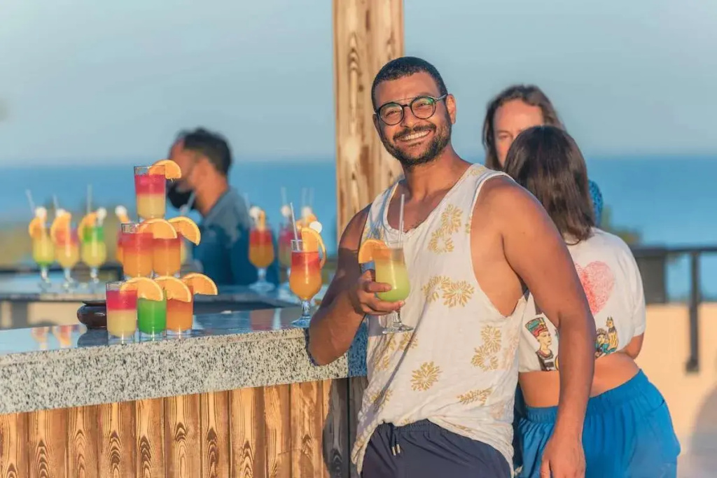 Prima Life Makadi Hotel - All inclusive: A lively seaside bar serves colorful drinks at a wood-fronted counter, with the sea visible behind.