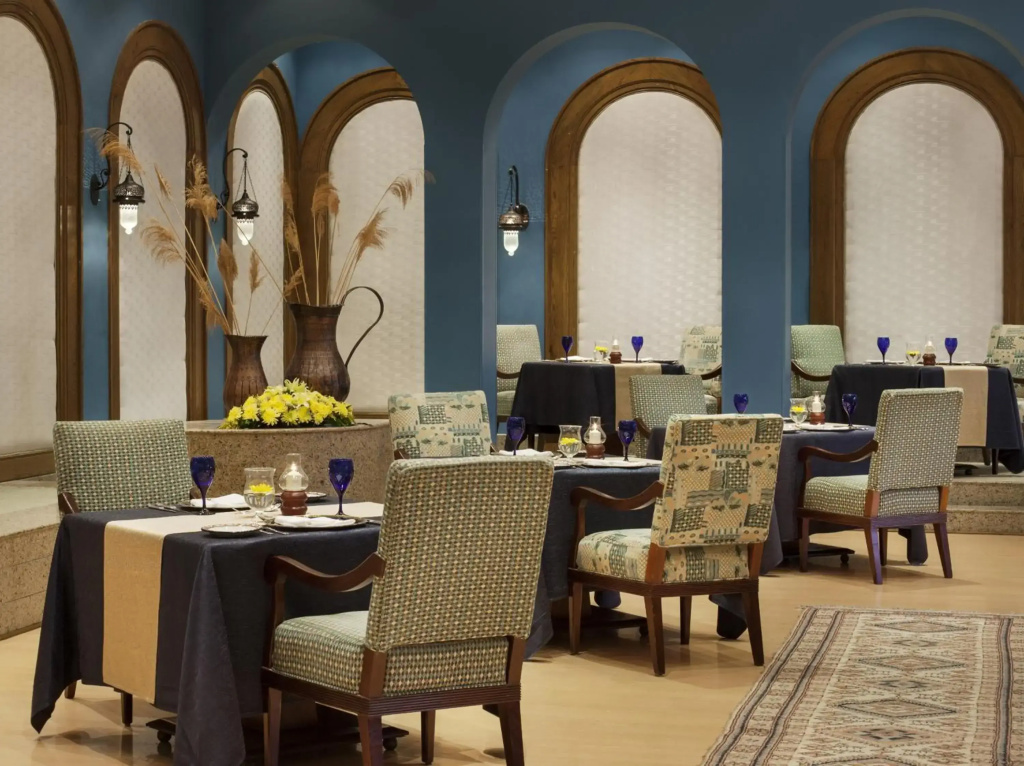 صورة: The Oberoi Beach Resort, Sahl Hasheesh: An elegant restaurant dining room with set tables, upholstered chairs, arched alcoves, and warm wall lighting.