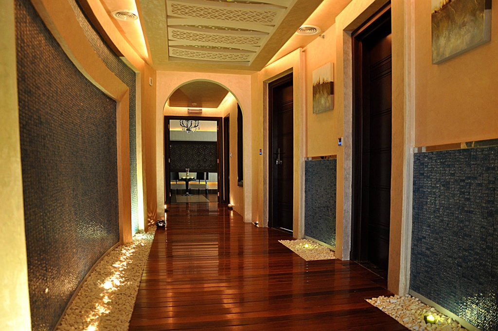 KaiSol Romance Resort Sahl Hasheesh (Adults Only): A warm, arched corridor with dark wood flooring, mosaic wall panels, and softly lit pebble borders.
