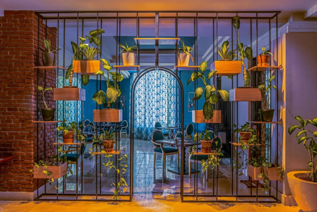 Rixos Sharm El Sheikh Ultra All Inclusive - Adults Friendly: A leafy indoor dining area with intimate tables and chairs behind a glass-and-metal partition.