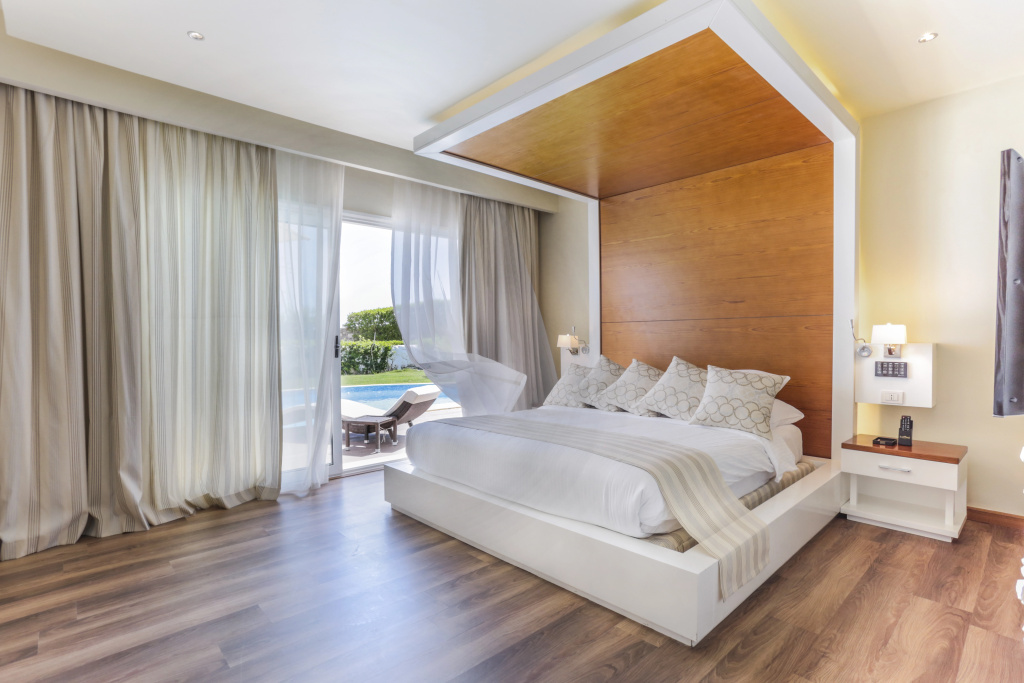 SUNRISE Montemare Resort - Grand Select: Bright bedroom with a king bed, floor-to-ceiling curtains, and glass doors opening onto a patio beside a swimming pool.