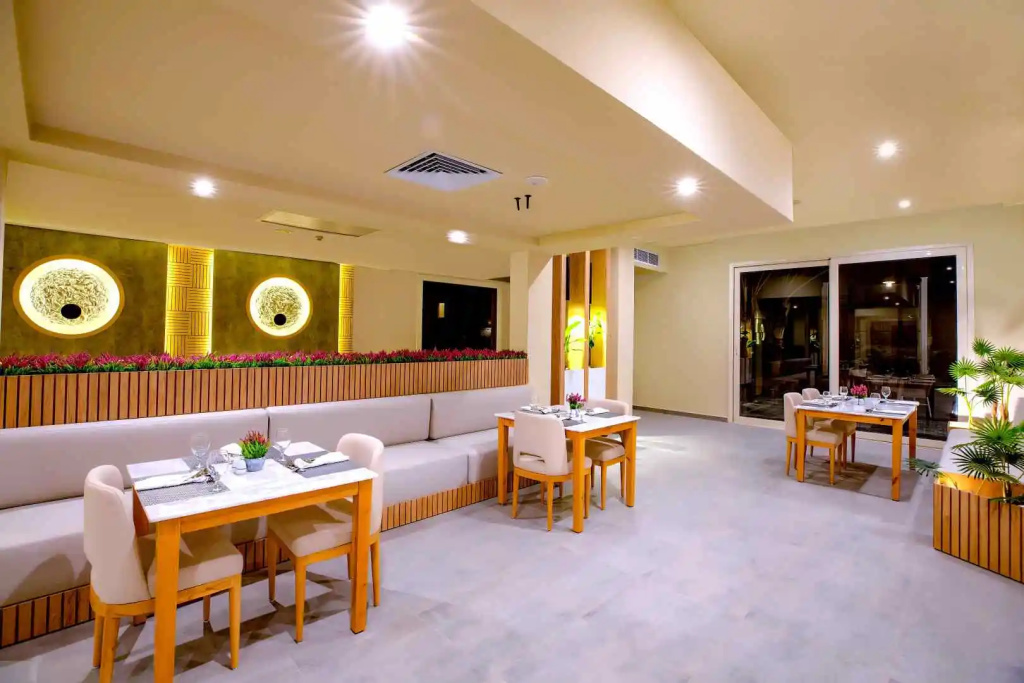 AJIRA Resort Sahl Hasheesh: Bright indoor dining area with tables, upholstered chairs, and a long banquette.