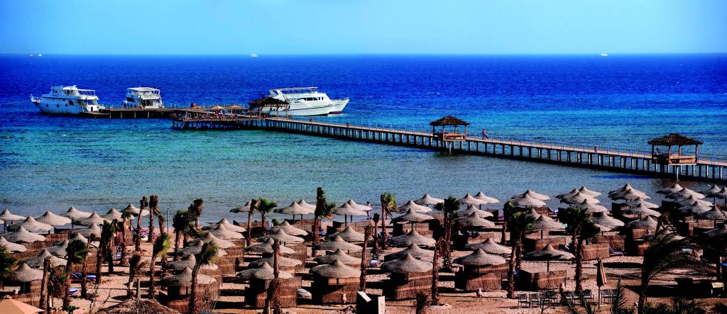 Amwaj Beach Club Abu Soma: A sandy beachfront lined with shaded loungers, with a long pier extending over the blue sea.